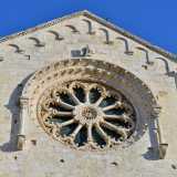 Al centro si inserisce il particolare rosone a doppia raggiera, posto tra due colonnine dai capitelli a motivi vegetali su cui si imposta un arco a tutto sesto finemente scolpito con foglie e fiori
